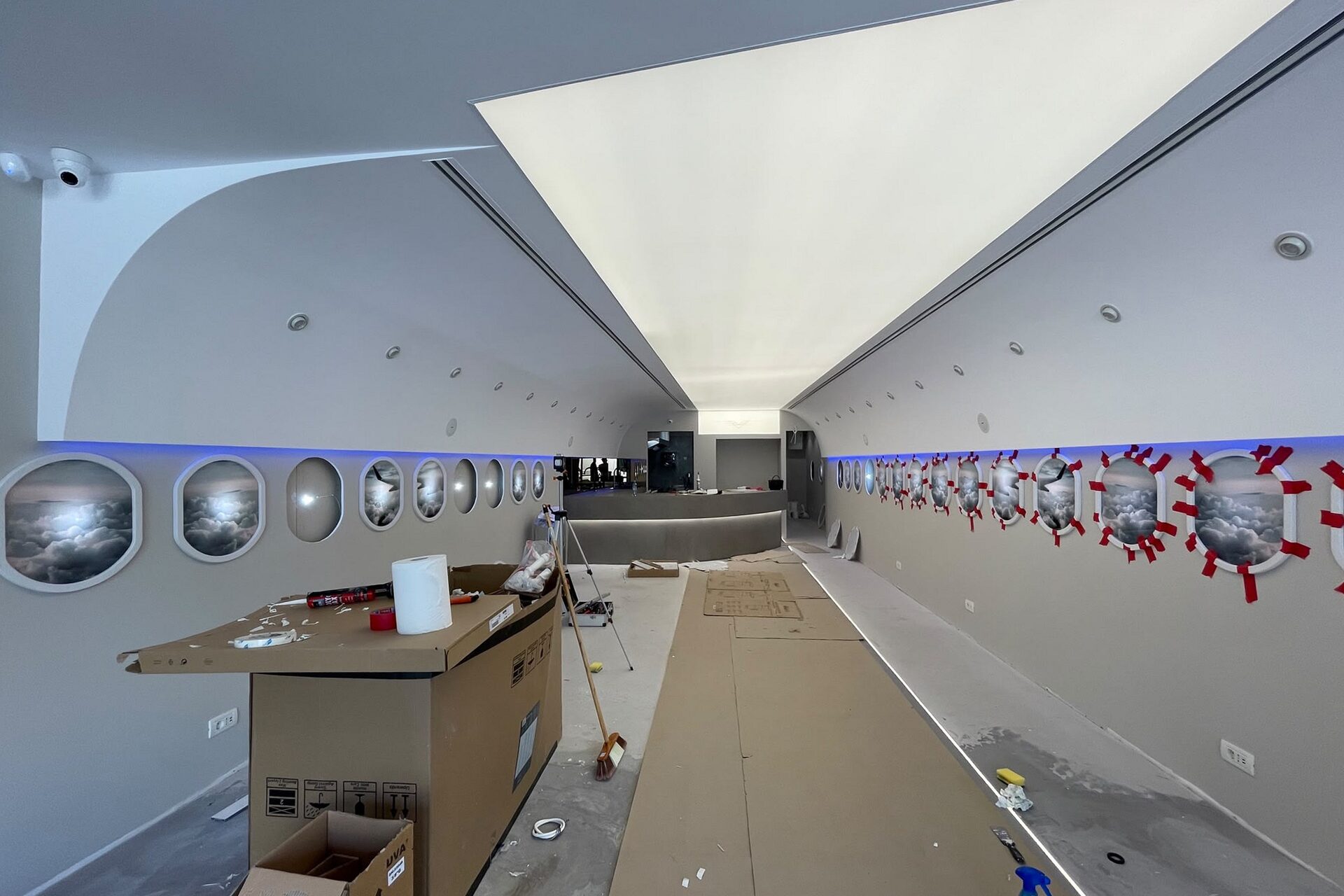 The cabin volume taking shape: full-length ceiling arc and lit cove in place, glazed portholes on the left wall, red clamps still on the right-hand run, bar carcass at the far end.