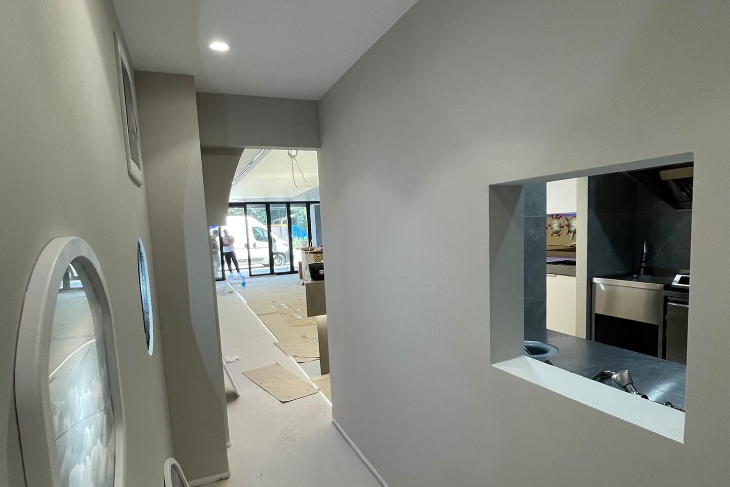 Back corridor near completion: an oval porthole set into the left-hand wall, service hatch cut through to the kitchen on the right, arched soffit leading back to the main room.