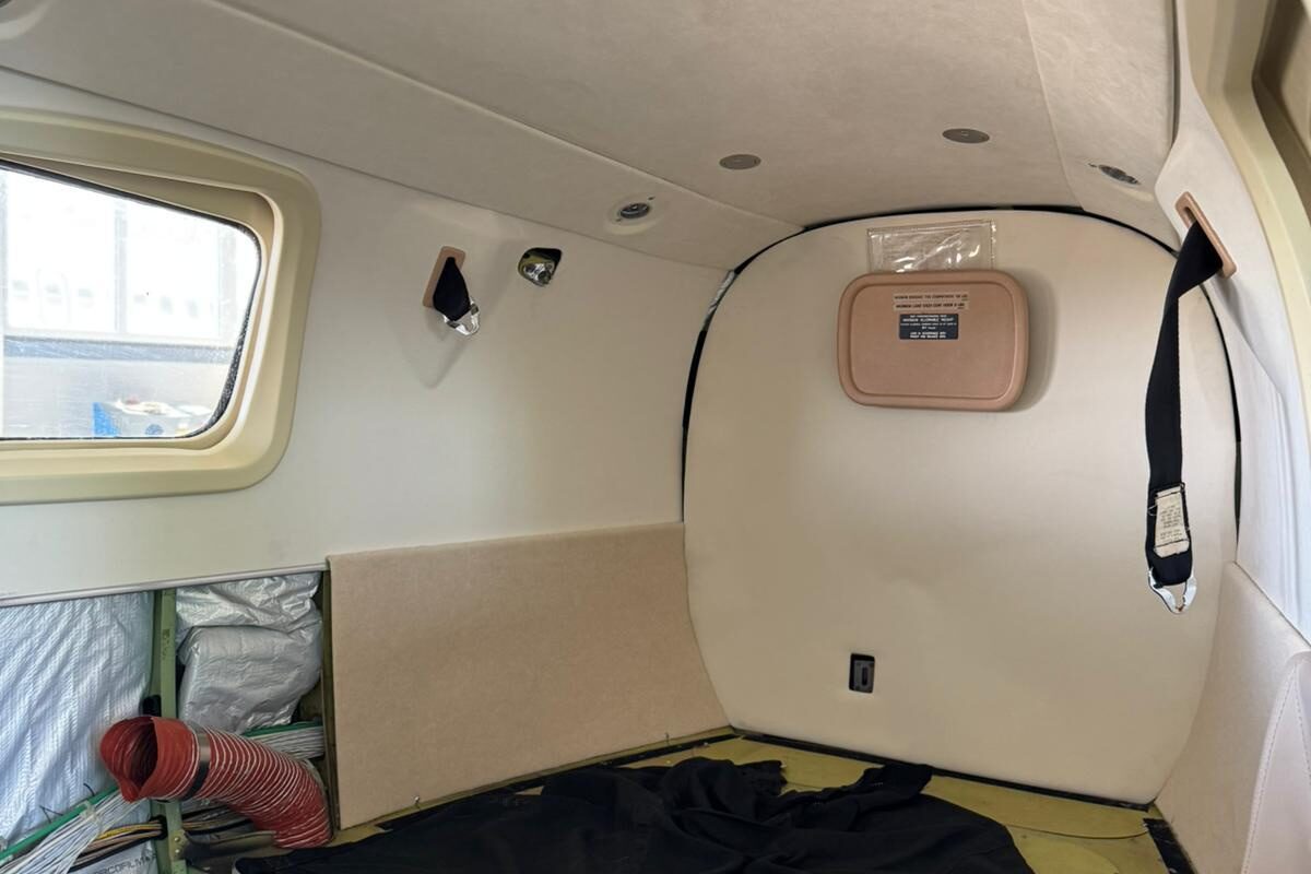 The cabin stripped back to structure: bare green zinc-chromate airframe and floor beams exposed below the window line, seats, carpet and lower sidewalls removed, ducting loose.