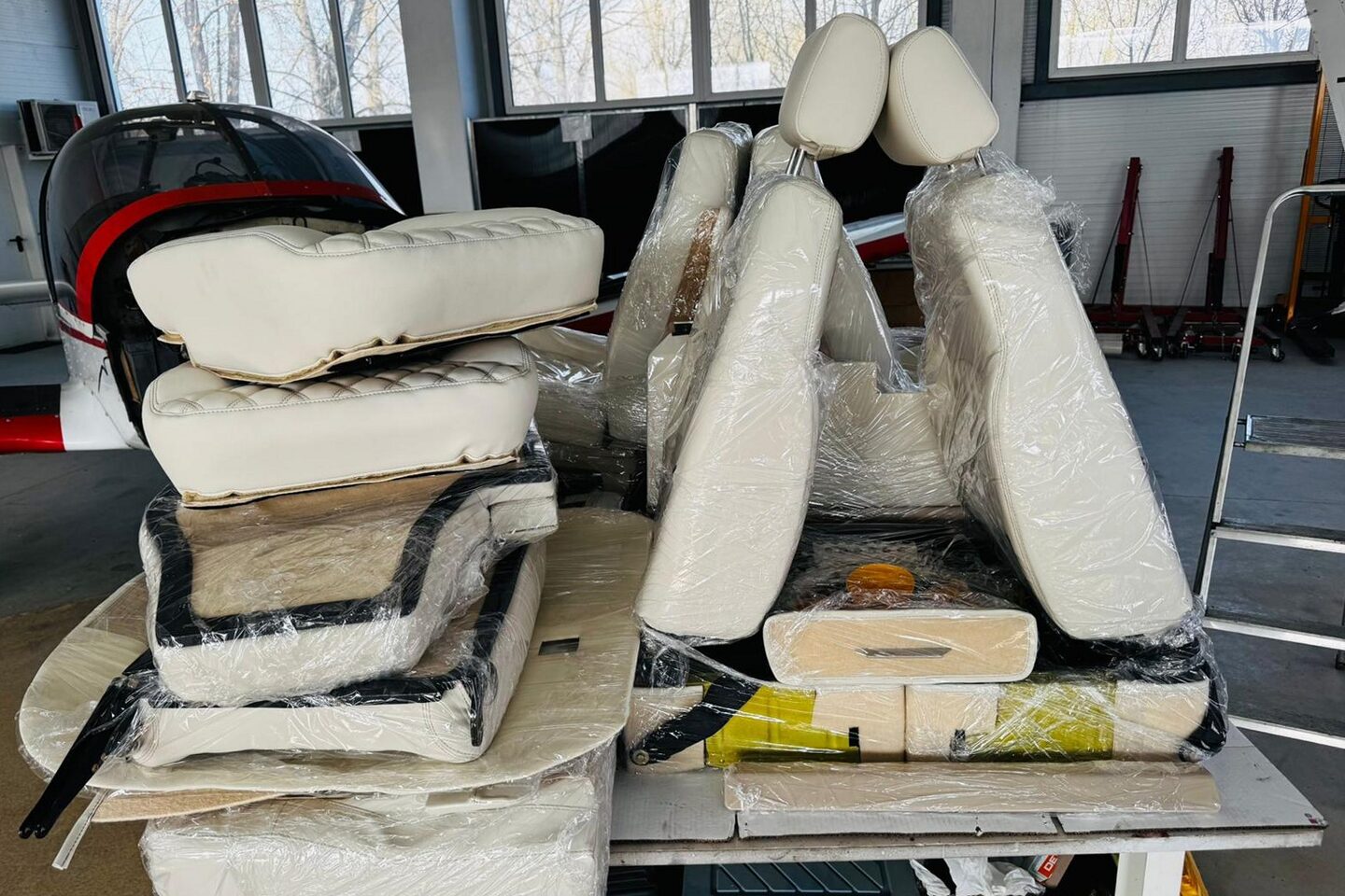 The original seats stripped out and stacked on the workshop bench: old foam squabs, bare seat pans and backs, new white leather sections wrapped in film alongside.