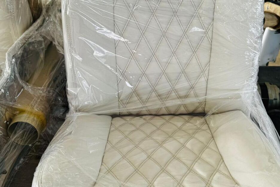 A finished seat still in protective film: white leather with diamond-quilted stitch across squab and backrest, Malibu script embroidered on the headrest.