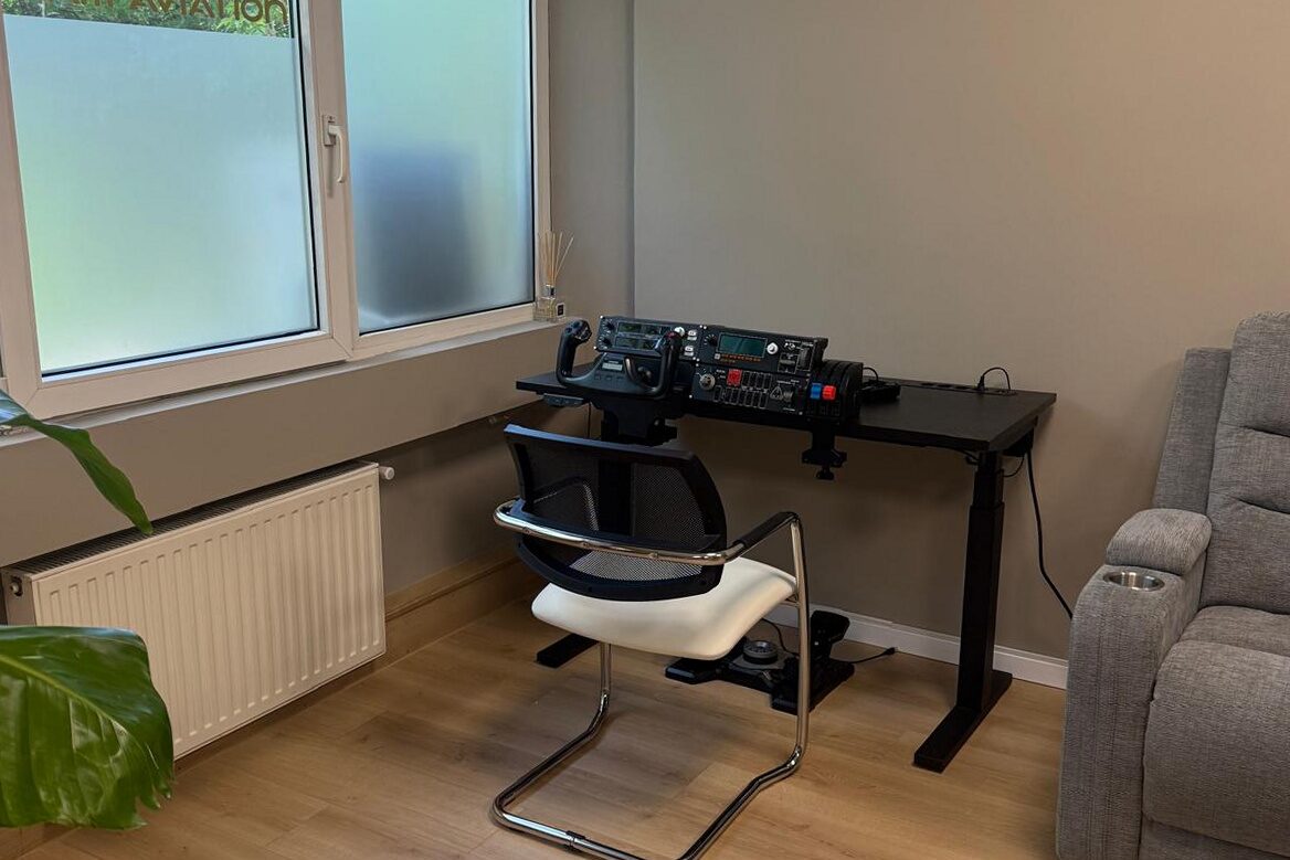 Corner workstation with a desk-mounted flight simulator yoke and throttle quadrant, white cantilever chair, RAM Aviation logo etched into the frosted window film behind, oak plank floor.